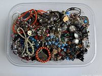 Top view of clear plastic bin densely packed with mixed costume jewelry pieces