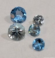 Five blue zircon gemstones arranged on white surface