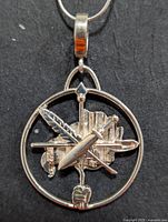 Front view of silver pendant showing crossed quill and sword inside circular frame
