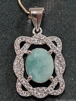 Front view of silver pendant showing emerald-colour centre stone and CZ border
