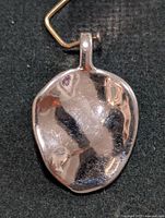 Front view of polished silver pendant with bail and gold-tone wire hook
