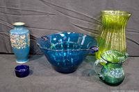 Group shot showing all six glass pieces: blue enamel vase, cobalt bowl, green ribbed vase, green pitcher, teal bowl, cobalt votive