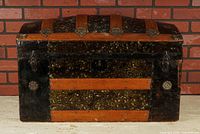 Front view of humpback steamer trunk showing wood slats, embossed tin panels, latches and lock