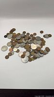 Pile of assorted copper, bronze and nickel world coins on white surface