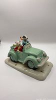 Angled view of glazed ceramic figurine showing Rupert and Bill in mint-green car on cream base