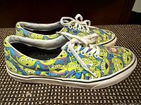 Side profile of both sneakers showing Toy Story alien glow-in-the-dark print and white laces