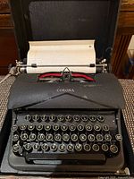 Typewriter in case with paper inserted showing keys and ribbon