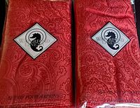 Front view of two sealed packs of red Waterford Linens napkins showing logo tag