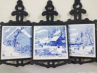 All three Currier & Ives cast iron porcelain tile trivets side by side