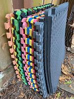 Stack of multicolour and black interlocking EVA floor tiles leaning against fence