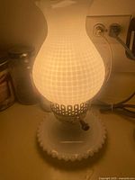 Lamp lit showing milk glass hobnail shade, metal collar, base, cord