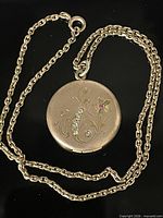 Full view of gold-tone floral locket on chain