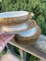 Stack of six plates beneath small gilt floral tureen