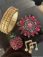 Group shot showing stretch bracelet, apple brooch, starburst brooch and pair of musical note pins