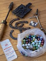 Overview of lot showing marbles, horseshoes, bridle bit, trivet, tool, dice, badge