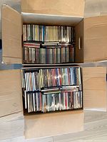 Two open cardboard boxes filled with rows of CD jewel cases