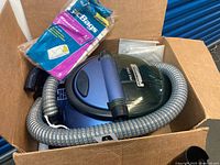 Open box showing blue Kenmore canister vacuum, flexible hose, pack of Kenmore Style M bags