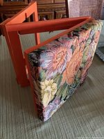 Footstool folded showing tapestry top and orange frame