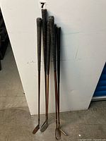 Six wooden-shaft golf clubs leaned against wall