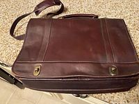 Front view of brown leather messenger bag with flap closed showing brass turn-lock closures and shoulder strap