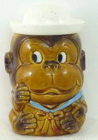 Front view of brown ceramic monkey head cookie jar with white hat lid