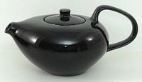 Side profile of glossy black teapot showing handle, spout and lid.