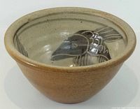 Oblique view of stoneware bowl showing brown exterior and glazed interior with fish motif