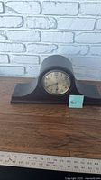 Full view of wooden tambour mantel clock on table with ruler for scale