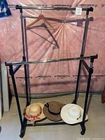 Garment rack assembled with three hats on base shelf and wooden hanger on top rail