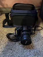 Front view of Panasonic Lumix DMC-FZ20 with lens cap, neck strap and camera bag in background