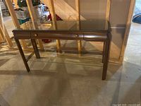 Full view of wood console table with glass top, two drawers, lower glass shelf