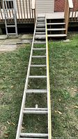 Full view of extended aluminum ladder on lawn with tape measure