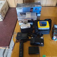 Overview of boxed Coby alarm clock, Electrohome clock, Sony Walkman, cameras, charger, trimmer on table