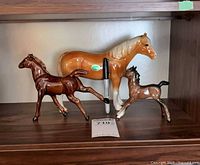 All three ceramic horse figurines on shelf with marker for scale
