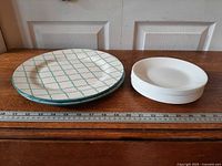 Stack of three Baum dinner plates next to six Corelle bread plates with ruler for scale