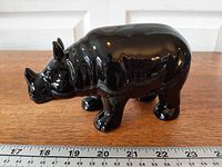 Side view of black ceramic rhinoceros with ruler for scale