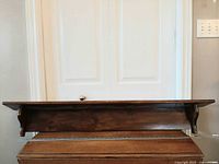 Front view of full-length dark wooden wall shelf mounted for display