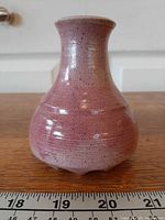 Front view of pink pottery bud vase next to ruler