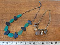 Both necklaces laid out beside ruler for scale