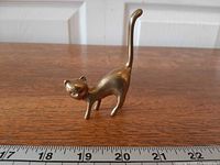 Full view brass cat ring holder beside ruler