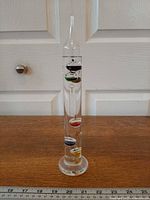 Full view of Galileo thermometer standing on wooden surface with ruler for scale