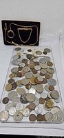 Tray with large assortment of foreign coins, jewelry case above containing watch chain and tie clips