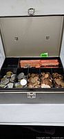 Open metal cash box showing coin tray with rolls and loose coins