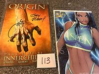 Both comic books side by side: Origin and Aspen