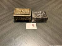 Both trinket boxes closed, brass-tone box on left, silver-tone on right