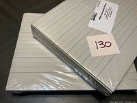 Two sealed packs of ruled newsprint paper stacked