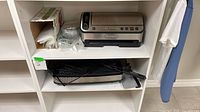 Vacuum sealer, bag roll box, loose rolls, and grill on shelving