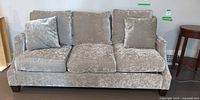 Front view of crushed velvet sofa showing three seat cushions, three back cushions, two throw pillows, dark block feet