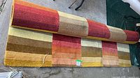 Rolled rectangular area rug showing multicolor gradient stripes