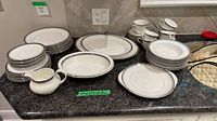Overall lot view showing stacked plates, cups, saucers, serving platter, vegetable bowl, creamer